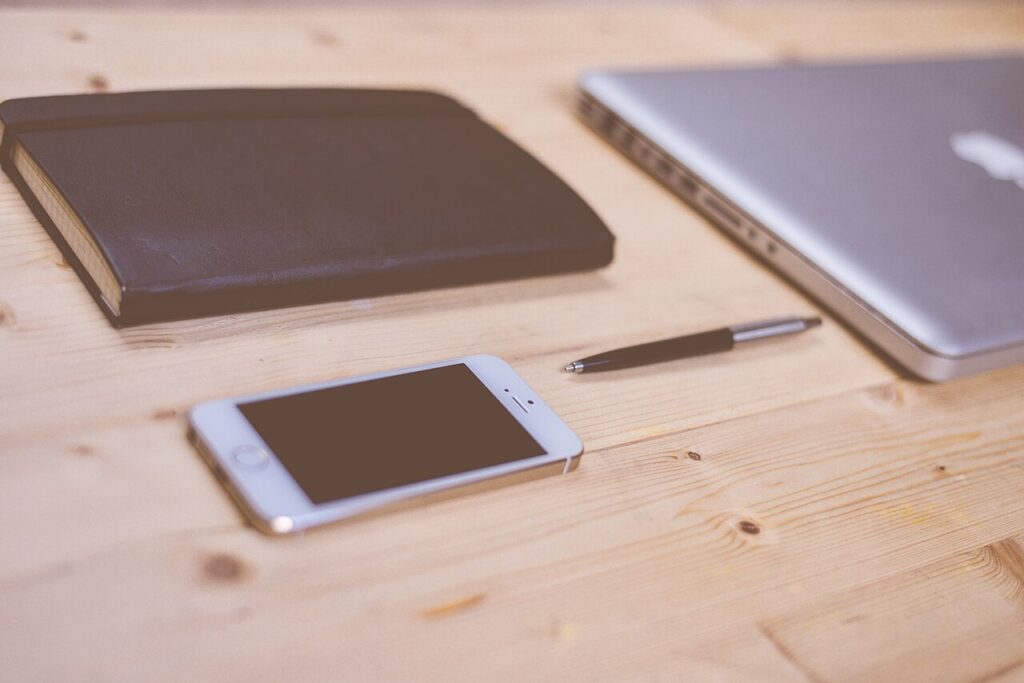 Smartphone on a wooden desk beside a notebook, pen and closed laptop