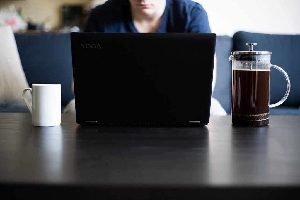 Person using a laptop at a coffee table beside a mug and French press