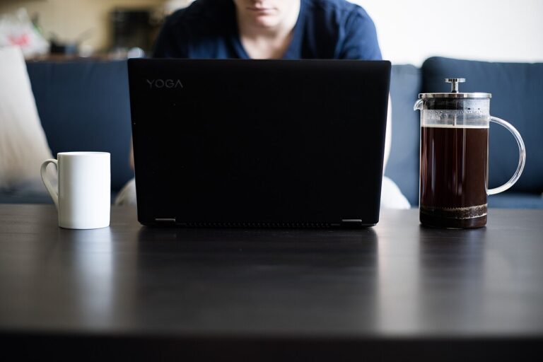 Person using a laptop at a coffee table beside a mug and French press